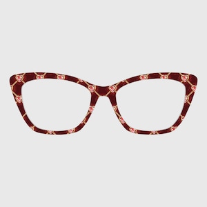 Op de afbeelding: Cat-eye bril met een donkerrood montuur voorzien van een herhalend patroon van kleine roze hartjes en dunne goudkleurige kettinkjes. Het ontwerp bedekt de gehele voorzijde van het montuur, dat een gladde en glanzende afwerking heeft.
