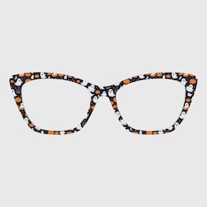 May include: Cat-eye glasses frames featuring a dark navy blue background with a repeating pattern of small white ghosts and orange pumpkins. The frames have a distinct pointed upper corner design and a smooth finish across the entire surface.