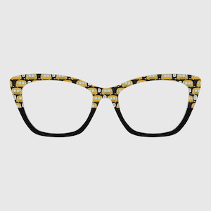 May include: Cat-eye eyeglasses with a black frame and a pattern of yellow school buses on a black background. The lenses are clear. The glasses have a retro, playful design.