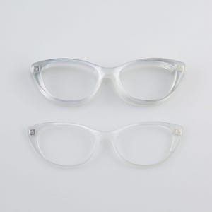 May include: Two pairs of clear, cat-eye shaped eyeglasses. The frames are transparent and appear to be made of plastic. The glasses are set against a plain white background, highlighting their sleek design and shape.