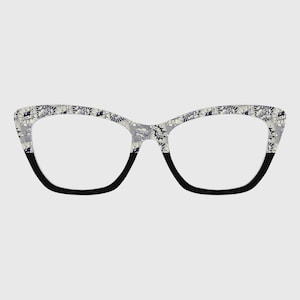 Puede incluir: Gafas de estilo ojo de gato con un patrón de cómic gris y blanco en las monturas. La parte inferior de las monturas es negra. Las lentes son transparentes.