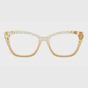 May include: Cat-themed eyeglasses with a light blue and yellow checkered pattern. The frames feature a gradient from light to a warm beige. Adorned with star and cat illustrations, these glasses offer a whimsical touch to eyewear.