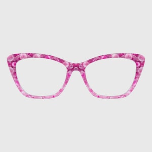 Puede incluir: Gafas de estilo ojo de gato con una montura de color rosa vibrante decorada con un patrón repetitivo de burbujas translúcidas en varios tonos de rosa y blanco. El diseño cubre toda la parte frontal de la montura, creando un aspecto colorido.