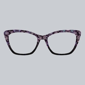 May include: Cat-eye style eyeglasses with a dark purple frame decorated with white and pink snowflakes. The frame fades to black at the bottom. The lenses are clear.