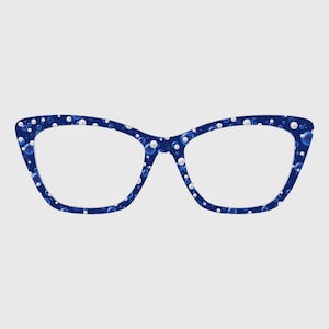 Puede incluir: Gafas de ojo de gato con una montura azul oscuro decorada con un patrón de esferas blancas de varios tamaños y burbujas azules translúcidas. El diseño cubre toda la parte frontal de la montura, creando una textura visual consistente.