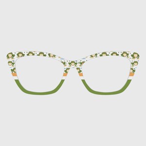 May include: Cat-eye style eyeglasses with a white frame featuring a pattern of green frogs. The lower frame is green, with orange and white stripes. The lenses are clear.