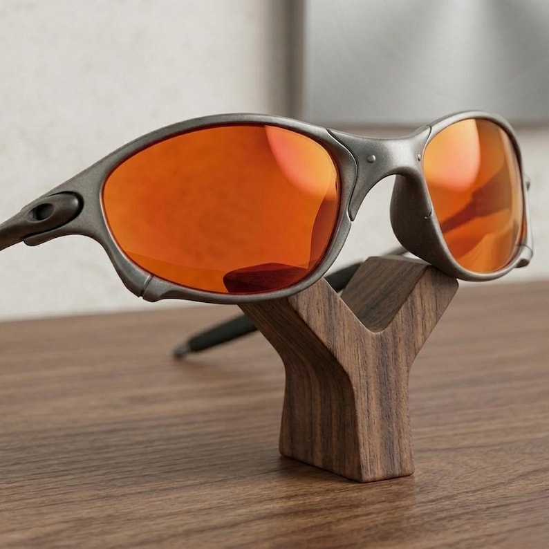 Op de afbeelding: Grijze zonnebril met oranje glazen op een houten standaard. De zonnebril heeft een modern design. De standaard is een donkerbruine, Y-vormige structuur.