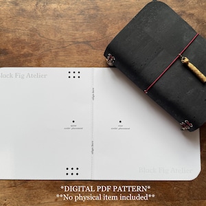 May include: A black cork journal with a red elastic closure and a gold-colored charm, next to a white paper template. The template has the text "Black Fig Atelier" and dotted lines. The text "DIGITAL PDF PATTERN" is also visible.