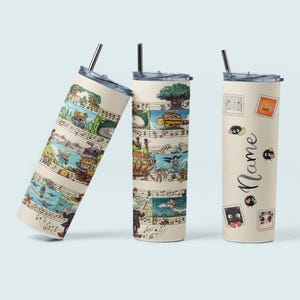 May include: Three beige stainless steel tumblers with illustrations of animated characters and musical notes. One tumbler has the word "Name" in a script font. Each tumbler has a silver straw and a lid.