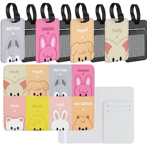 May include: A collection of luggage tags and a passport holder. The tags feature cartoon animal faces in various colors, including gray, pink, and beige, with black straps. The passport holder is white.
