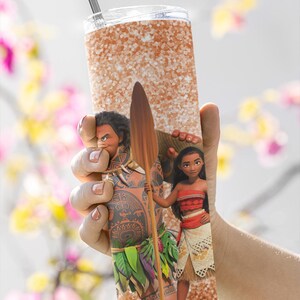 May include: A stainless steel tumbler with a glittery orange background and a design featuring characters from the animated film Moana. The tumbler includes a straw and a clear lid. The characters include Maui and Moana.