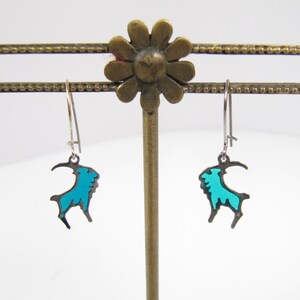 May include: A pair of silver dangle earrings with a turquoise blue goat silhouette charm.