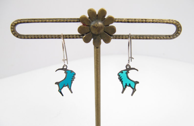 May include: A pair of silver dangle earrings with a turquoise blue goat silhouette charm.