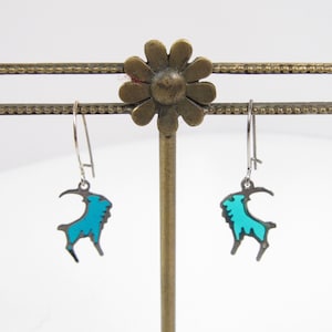 May include: A pair of silver dangle earrings with a turquoise blue mountain goat design.