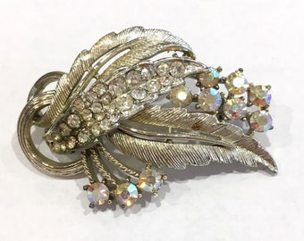 May include: A silver tone brooch with a leaf design and clear and iridescent rhinestones.
