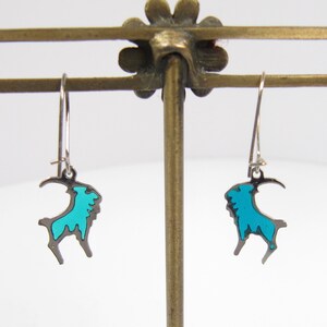 May include: A pair of silver dangle earrings with a turquoise blue goat design.
