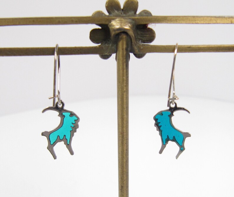 May include: A pair of silver dangle earrings with a turquoise blue goat design.