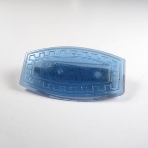 May include: A light blue glass button with a decorative border. The button has a slightly textured surface.