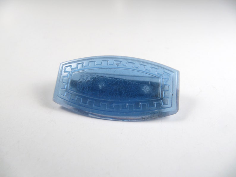 May include: A light blue glass button with a decorative border. The button has a slightly textured surface.