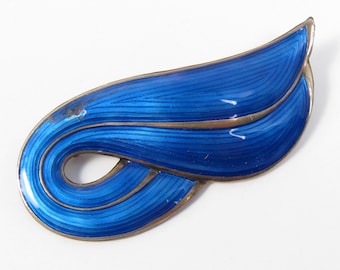 May include: A blue enamel and sterling silver brooch in the shape of a stylized leaf. The brooch has a smooth, shiny finish and is decorated with delicate lines.