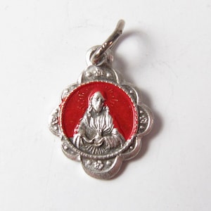 May include: Silver charm with a red enamel background featuring a depiction of Jesus Christ holding a chalice. The charm has a scalloped edge and a loop for attaching to a chain.