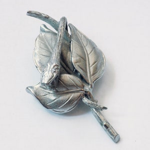 Op de afbeelding: Zilveren broche met een gestileerde slang die om drie bladeren is gewikkeld. De bladeren zijn getextureerd en hebben een realistisch uiterlijk.