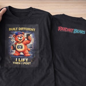 Może przedstawiać: Czarny t-shirt z kreskówkowym misiem z aparatem i telefonem, z napisem "BUILT DIFFERENT, I LIFT THEN I POST". Z tyłu koszulki napis "RATCHET BEARS" w kolorze czerwonym i niebieskim.