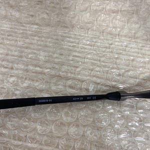 May include: Black eyeglasses frame with the text "006019-01", "42-29", and "151 CE". The frame is resting on a surface with a bubble wrap pattern.