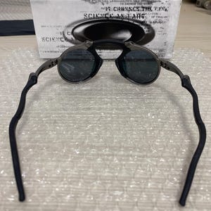 May include: Dark gray sunglasses with round lenses and black temples. The glasses are set against a white box with the text "SCIENCE AND ART". The temples have a curved design for a comfortable fit.