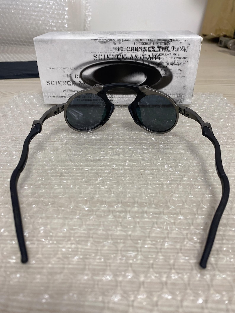 May include: Dark gray sunglasses with round lenses and black temples. The glasses are set against a white box with the text "SCIENCE AND ART". The temples have a curved design for a comfortable fit.
