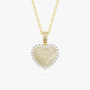 May include: A gold-colored necklace with a heart-shaped pendant. The pendant is encrusted with small, clear gemstones and has a border of larger, clear gemstones. The chain is also gold-colored.