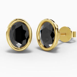May include: A pair of stud earrings featuring oval-cut black stones set in polished yellow gold bezels. Each earring has a smooth, rounded gold frame surrounding the faceted black center, complete with a gold post and a secure backing mechanism.