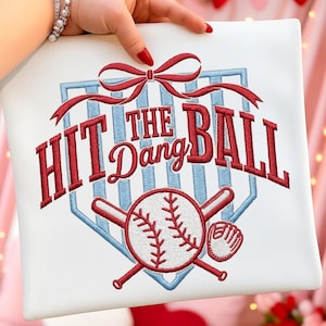Könnte beinhalten: Weißes Baseball-Design mit dem Text "HIT THE DANG BALL" in roter Stickerei. Das Design umfasst einen Baseball, gekreuzte Schläger und einen Baseballhandschuh, alle in Rot. Oben befindet sich eine rote Schleife.