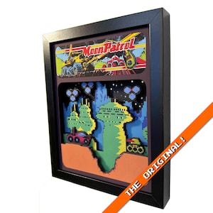 Może przedstawiać: Oprawiona grafika przedstawiająca scenę z gry wideo retro. Górna część przedstawia "Moon Patrol" z żółtym pojazdem. Dolna część przedstawia pikselowy krajobraz z pojazdami i strukturami. Rama jest czarna, z pomarańczowym banerem z napisem "THE ORIGINAL!"