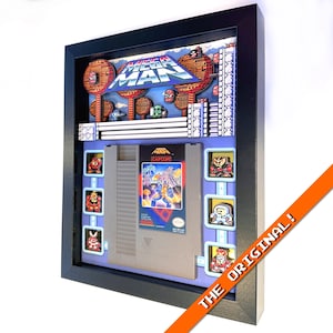 May include: Framed artwork featuring a classic video game cartridge. The artwork includes a 3D diorama of the game's environment and characters, with the game cartridge prominently displayed. The frame is black, and the background is blue. The text "THE ORIGINAL!" is on an orange diagonal stripe.