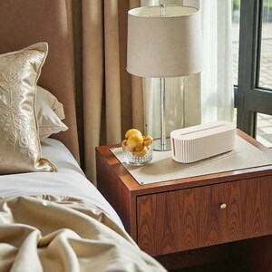 K&ouml;nnte beinhalten: Ein Nachttisch aus Holz mit einer Lampe, einer dekorativen Box und einer Glasschale mit Obst. Der Tisch hat eine Schublade mit einem goldenen Knopf. Ein beigefarbener Lampenschirm sitzt auf einem silbernen Lampenfu&szlig;. Eine dekorative, cremefarbene Box befindet sich auf dem Tisch.