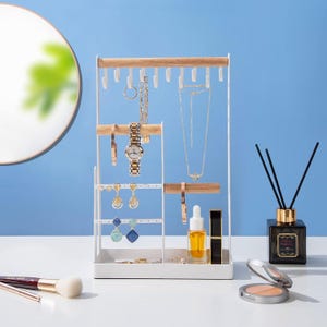 May include: A white and wood-toned jewelry organizer with various necklaces, earrings, and a watch displayed. The organizer has multiple levels and hooks for hanging jewelry. Other items include makeup and a fragrance diffuser.
