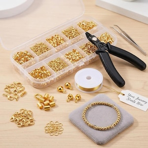 May include: A jewelry making kit containing a clear plastic organizer box filled with gold-toned metal findings, a pair of black-handled pliers, silver-toned tweezers, a spool of gold wire, and a white tag with the text Your Journey Starts Here.