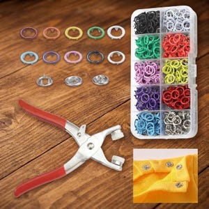 May include: A metal fastener plier tool with red handles, a clear plastic storage container with ten compartments filled with assorted colorful metal pronged snap buttons, and a yellow fabric swatch with four installed silver snap buttons.