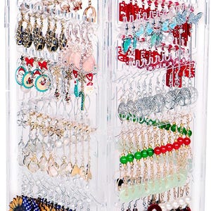 May include: Clear acrylic earring display stand filled with various earrings. The earrings include red, white, and blue sunflower earrings, red heart-shaped earrings, and earrings with Christmas and Chinese New Year themes.