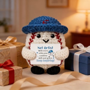 May include: A handmade baseball-themed plushie with a blue hat and red stitching. The plushie holds a card that reads "Net Artist" with an inspirational message. The background includes wrapped gifts with ribbons, suggesting a celebratory theme.