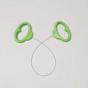 May include: A cake leveller featuring two light green plastic handles connected by a thin, flexible metal wire. The wire is curved into a loop, and the handles are shaped with ergonomic grips for holding while slicing through baked goods.
