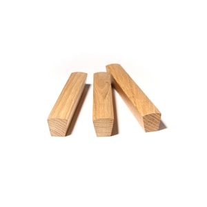 Op de afbeelding: Drie rechthoekige houten blokken met een natuurlijke houtnerf afwerking. Elk blok heeft een vierkante doorsnede en een licht afgeronde bovenkant. De blokken zijn op een witte achtergrond geplaatst.