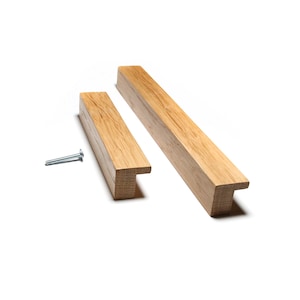 May include: Two wooden cabinet pulls with a natural wood grain finish. One pull is shorter than the other. A silver screw is next to the pulls. The pulls have a T-shaped design.