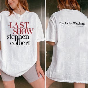 May include: White t-shirt featuring the text "the LAST SHOW with stephen colbert" in red and black. The back of the shirt displays "Thanks For Watching!" in black text. A casual, unisex tee.
