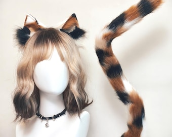 Könnte beinhalten: Ein Set aus Kunstfell-Katzenohren und einem langen, passenden Katzenschwanz mit einem dreifarbigen Muster in Schwarz, Weiß und Braun. Die Ohren sind an einem Haarreif befestigt und der Schwanz ist geschwungen. Ein schwarzes Halsband mit kleiner Glocke.