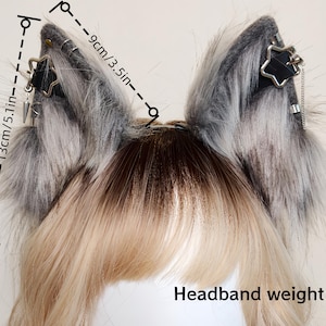 K&ouml;nnte beinhalten: Ein Haarreif mit Tierohren aus grau-wei&szlig;em Kunstfell, verziert mit schwarzen Riemen, silbernen sternf&ouml;rmigen Anh&auml;ngern und kleinen Metallketten. Die Ohren sind 13 cm hoch und 9 cm breit, das Gesamtgewicht des Haarreifs betr&auml;gt 60 Gramm.