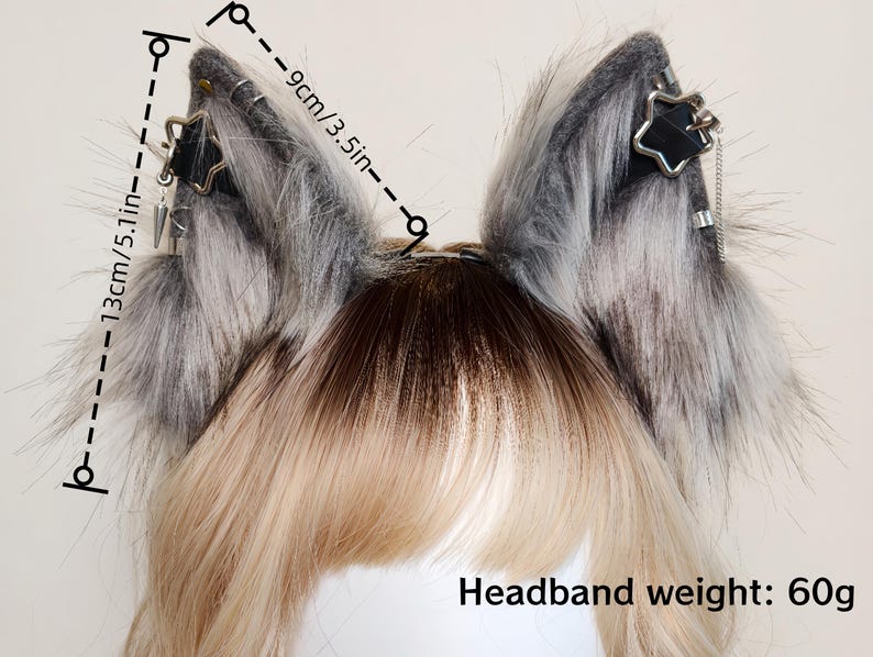 K&ouml;nnte beinhalten: Ein Haarreif mit Tierohren aus grau-wei&szlig;em Kunstfell, verziert mit schwarzen Riemen, silbernen sternf&ouml;rmigen Anh&auml;ngern und kleinen Metallketten. Die Ohren sind 13 cm hoch und 9 cm breit, das Gesamtgewicht des Haarreifs betr&auml;gt 60 Gramm.