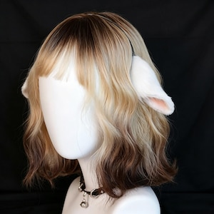 May include: A shoulder-length wavy wig featuring a dark brown to blonde ombre colour transition with bangs. The wig is styled with a black headband adorned with white, plush, rounded animal ears that have soft pink inner details. A black choker with a bell.