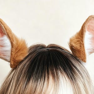 Pode incluir: Um par de orelhas de animal de pelúcia presas a uma tiara preta fina. As orelhas são cobertas por pele sintética castanha macia nas bordas externas, com pelo rosa claro e branco revestindo as seções internas, criando uma aparência realista.